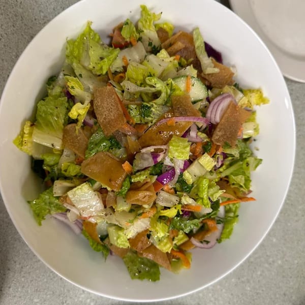 A vibrant Mediterranean fattoush salad in a white bowl, featuring fresh greens, cucumbers, red onions, and crispy pita bread.