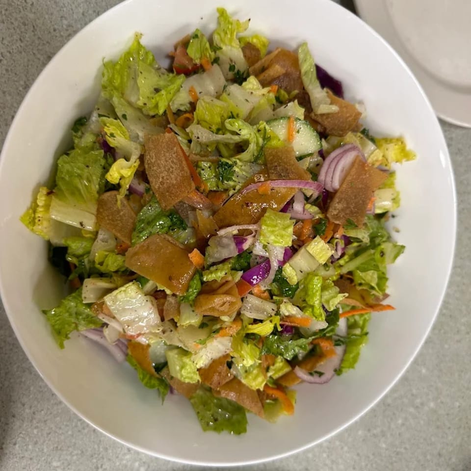 A vibrant Mediterranean fattoush salad in a white bowl, featuring fresh greens, cucumbers, red onions, and crispy pita bread.