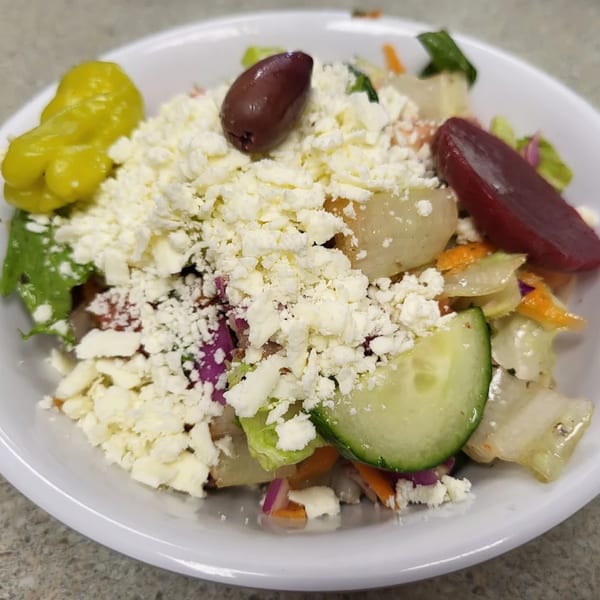 A vibrant Mediterranean salad with feta, olives, pepperoncini, cucumber, and beets in a white bowl.