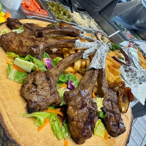 Grilled lamb chops with french fries and a side salad on a wooden platter at LaVie Mediterranean Grill.