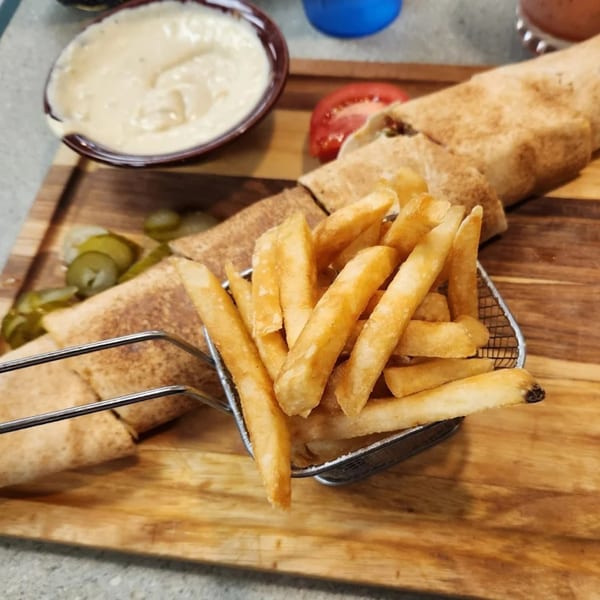 LaVie Mediterranean Grill's shawarma wrap, fries in a metal basket, dipping sauce, and pickles on a wooden board.