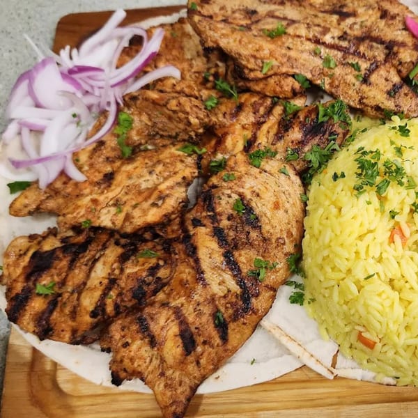 Grilled chicken with char marks, yellow rice, and sliced red onions on a wooden board.
